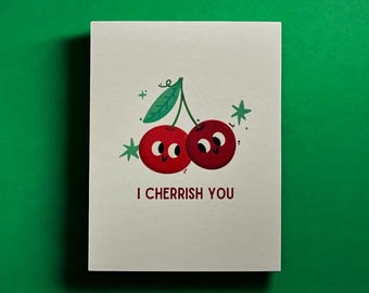 May include: A white greeting card with a green background features a cartoon illustration of two red cherries with smiling faces. The cherries have a green stem and leaf. The text "I CHERRISH YOU" is printed below the cherries.