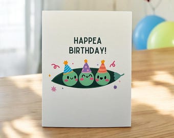 May include: A white card with the text "Happea Birthday!" and three green peas wearing party hats in a pea pod.