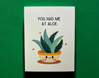 May include: A white card with the text "You had me at aloe." and a cartoon illustration of a green aloe plant in a yellow pot with a smiling face.
