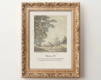 Puede incluir: Una impresión enmarcada con una ilustración vintage de ciervos en un bosque. La impresión incluye el texto "Salmo 42:1" y el versículo "Como el ciervo anhela las corrientes de agua, así mi alma te anhela a ti, oh Dios." La impresión está enmarcada en un marco ornamentado de color marrón claro.