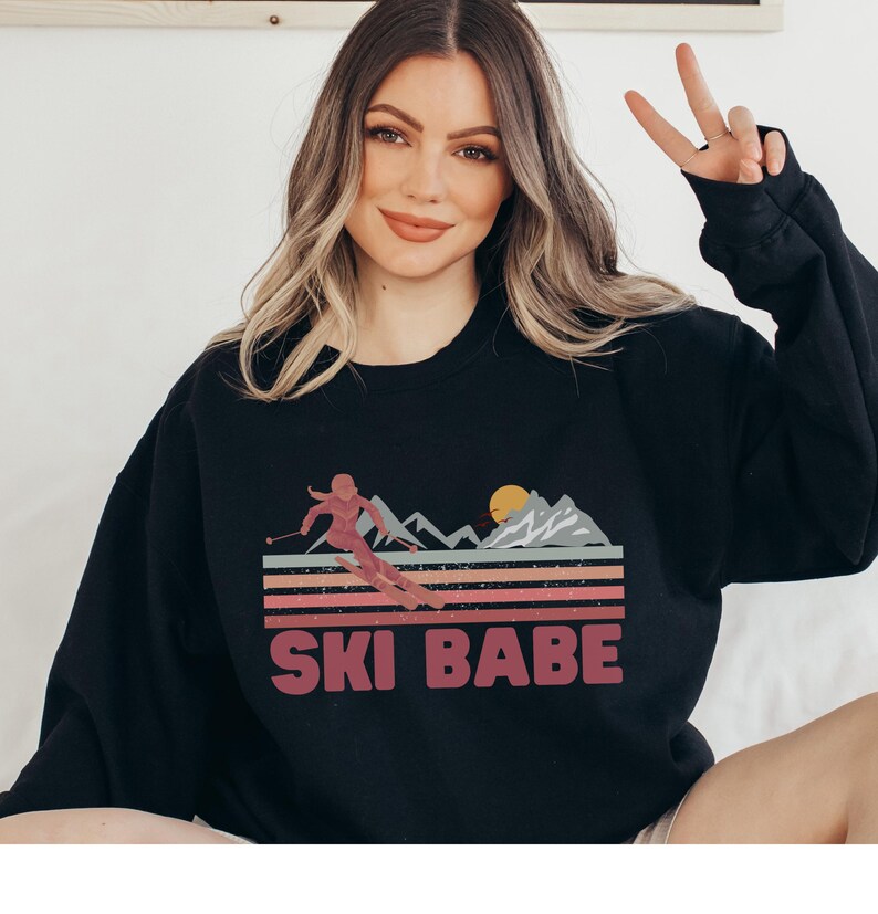 May include: Black sweatshirt with a retro-style graphic of a skier in a mountain landscape. The graphic includes the text "SKI BABE".