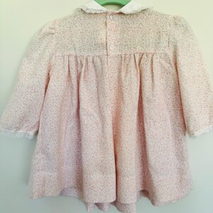 May include: A pink and white floral print dress with a white lace collar and cuffs. The dress has a button closure at the back.