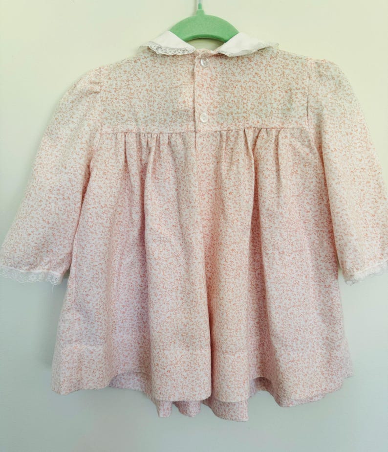 May include: A pink and white floral print dress with a white lace collar and cuffs. The dress has a button closure at the back.