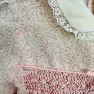 May include: A pink and white floral dress with a white lace collar and a pink smocked bodice.