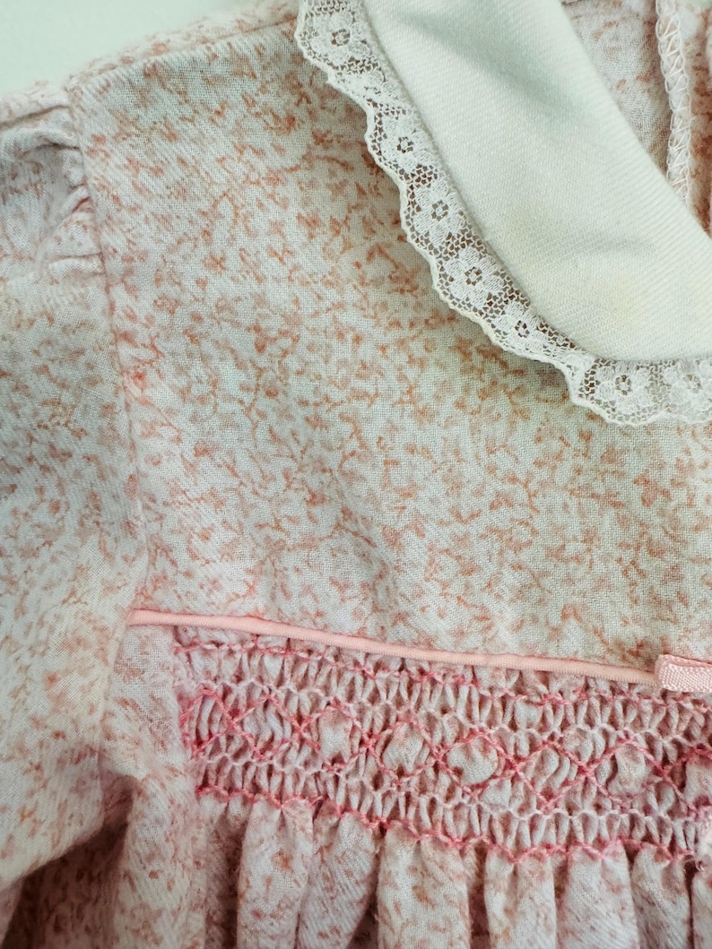 May include: A pink and white floral dress with a white lace collar and a pink smocked bodice.