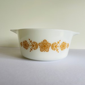 May include: White ceramic baking dish with a gold floral design. The dish has a rounded shape and two handles.