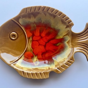 May include: A ceramic fish-shaped serving dish with a glossy finish. The dish features a brown exterior with a vibrant red and yellow interior. The fish has detailed fins and a tail, ideal for serving appetizers or snacks.