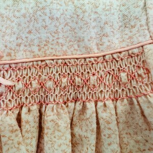 May include: A pink baby dress with a white floral pattern and a pink smocked detail around the waist.