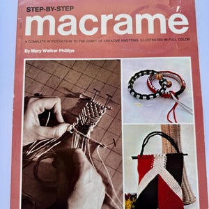 May include: A vintage book titled "Step-By-Step Macramé" with a red and white cover. The book features images of macramé projects, including bracelets and a tote bag. The cover also includes the author's name, Mary Walker Phillips.