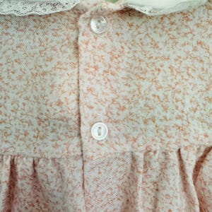 May include: A white collared dress with a lace trim and a small floral pattern. The dress has two white buttons on the front.