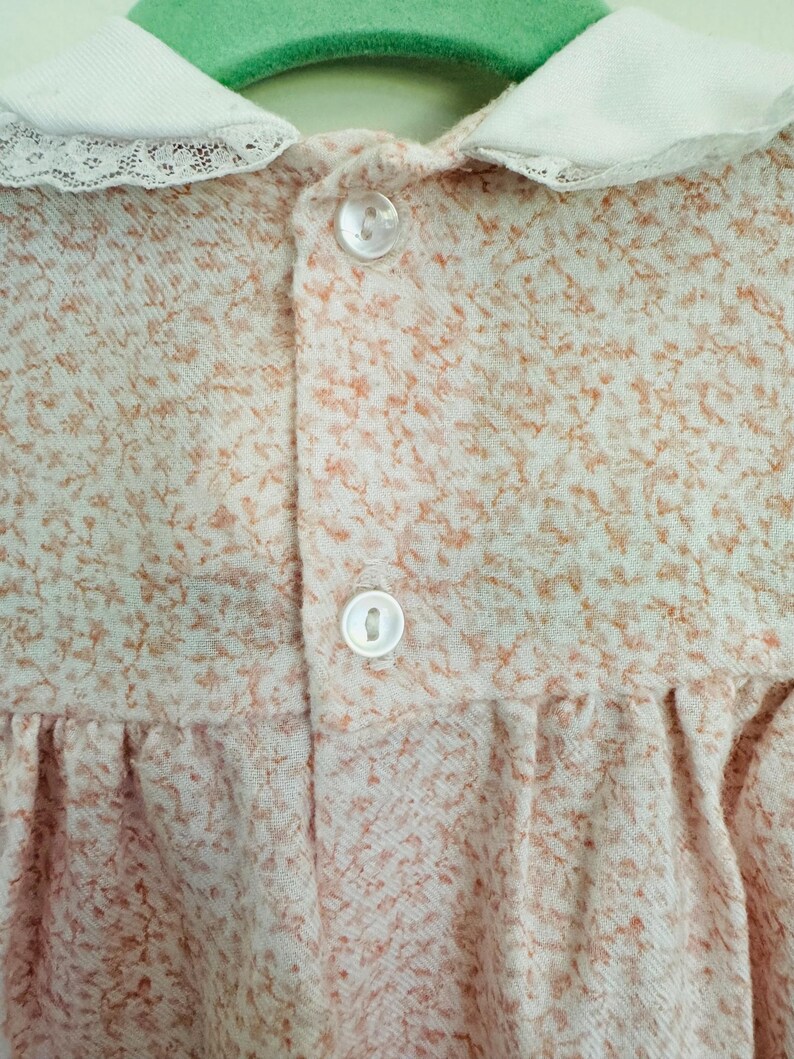 May include: A white collared dress with a lace trim and a small floral pattern. The dress has two white buttons on the front.