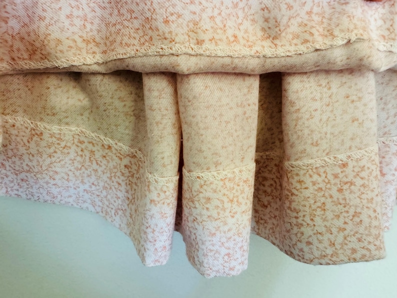May include: A close-up of a light pink skirt with a floral print. The skirt has a gathered hem and a scalloped edge.