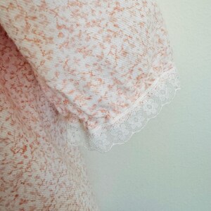 May include: A white dress with a pink floral pattern and lace trim on the sleeves.