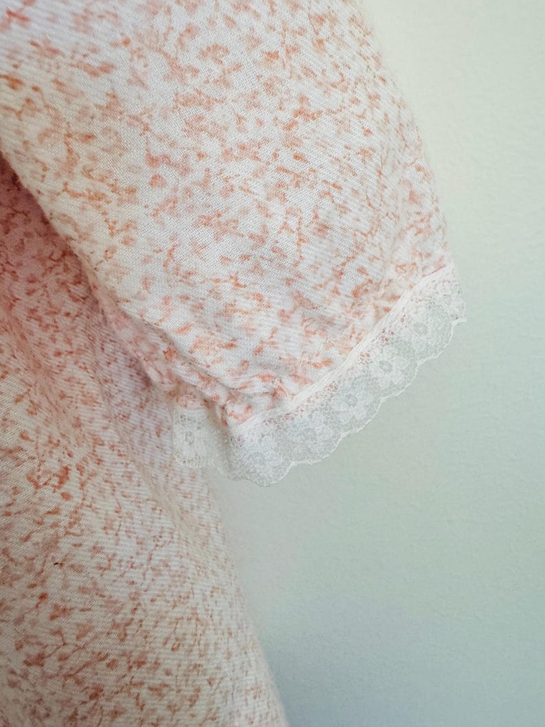 May include: A white dress with a pink floral pattern and lace trim on the sleeves.