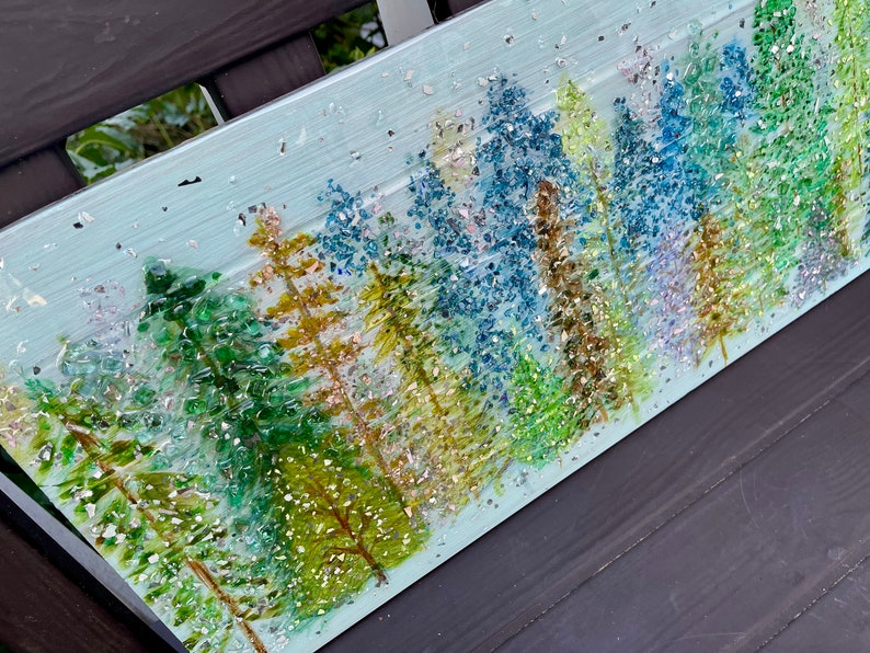 K&ouml;nnte beinhalten: Ein blaues und gr&uuml;nes Mosaik-Kunstwerk, das eine Waldszene darstellt. Die B&auml;ume bestehen aus kleinen Glassplittern und Glitzer, was einen funkelnden Effekt erzeugt. Der Hintergrund ist hellblau, und kleine wei&szlig;e Punkte sind &uuml;ber das gesamte Werk verteilt.