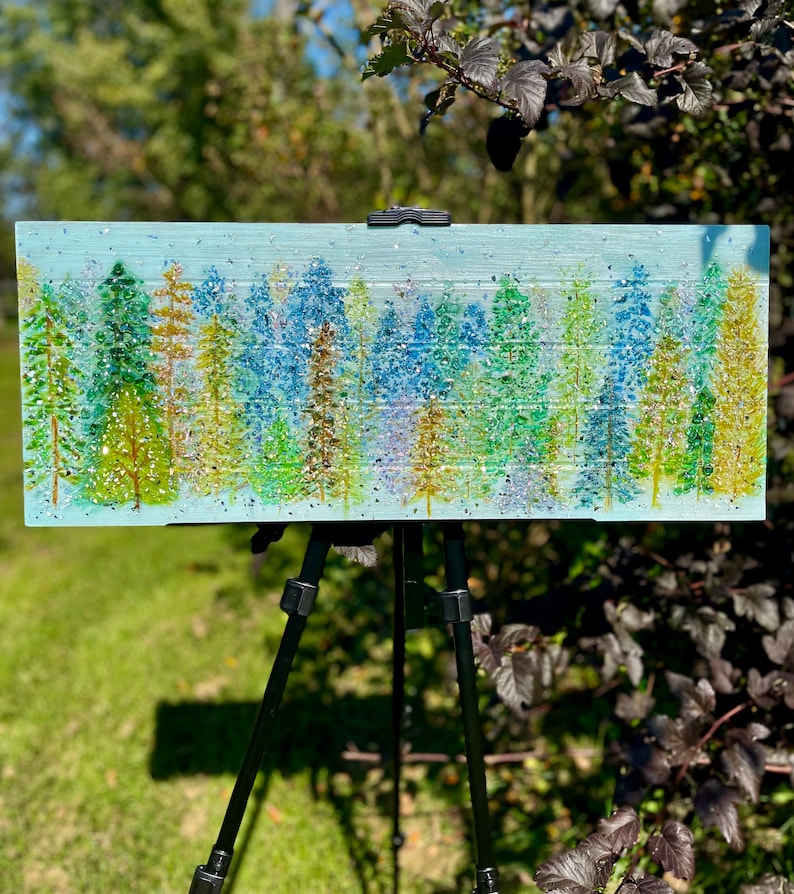 This is a beautiful 28x11 cedar wood board, painted with acrylic paints in the style of a pine forest. There are assorted trees that have a fire glass, crushed glass and glass ice application. The piece is then covered with resin coating.