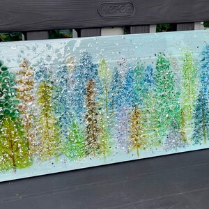 K&ouml;nnte beinhalten: Ein Glaskunstwerk, das eine Waldszene mit einer Vielzahl von blauen, gr&uuml;nen und goldenen B&auml;umen darstellt. Der Hintergrund ist hellblau mit einem subtilen Glitzereffekt.