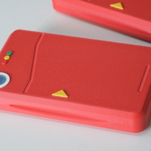 May include: Two red handheld game consoles with yellow and coloured buttons. The consoles have a rectangular shape with rounded edges. One console has a blue circle button and three small coloured buttons.