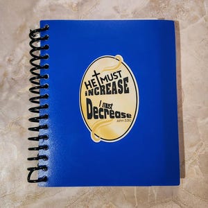 May include: A blue spiral notebook with a yellow sticker that says "He must increase, I must decrease, John 3:30".