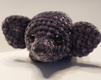 May include: A plush gray crocheted elephant toy with black eyes. The elephant has a textured, fuzzy surface.