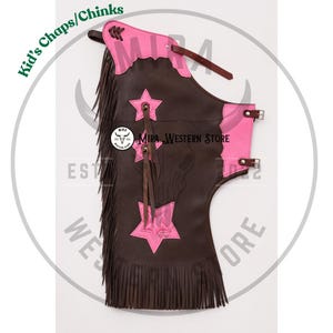 May include: Dark brown leather chaps for children featuring bright pink star-shaped overlays and trim. The chaps include long brown fringe along the side, adjustable leather straps with metal buckles, and decorative stitching. The text Kid's Chaps/Chinks is visible.