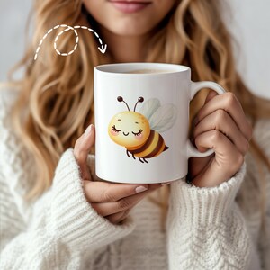 May include: White ceramic mug with a cartoon bee illustration. The bee is yellow and black with closed eyes and a smile. The mug has a handle.