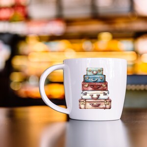 May include: White ceramic mug with a colorful illustration of a stack of vintage suitcases. The suitcases are painted in shades of blue, red, brown, and beige.