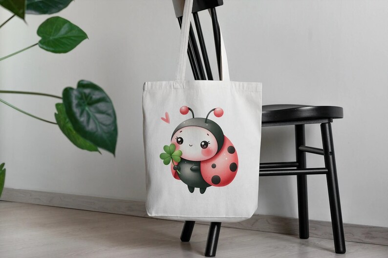 Puede incluir: Bolsa de tela blanca con una mariquita de dibujos animados sosteniendo un tr&eacute;bol de cuatro hojas. La mariquita tiene manchas negras y una concha roja.