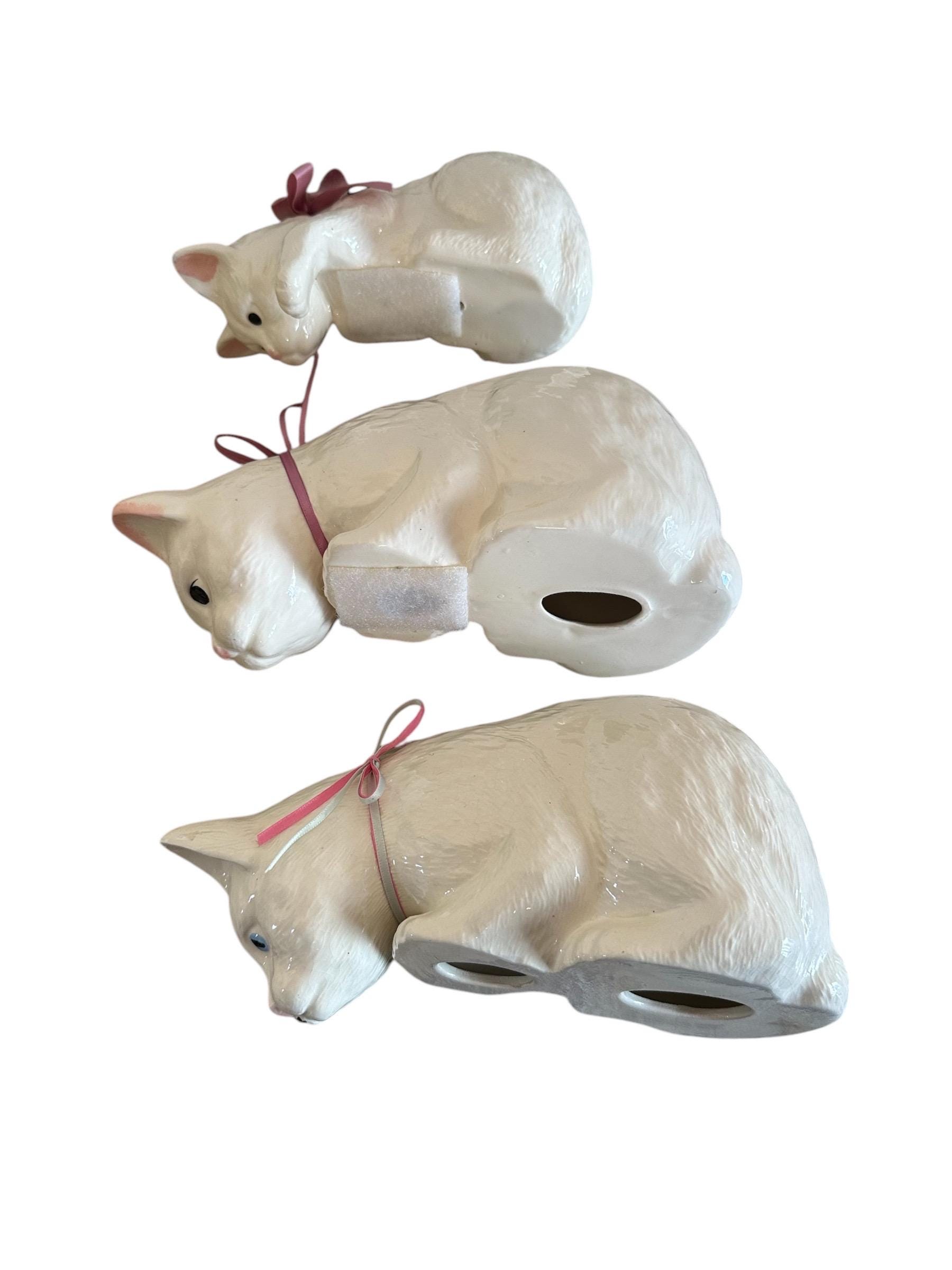 A Family of Three White Ceramic Cats Peeping Over the Edge