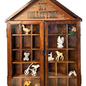 May include: A wooden display cabinet with glass doors, housing various miniature figurines. The cabinet is labeled "MY COLLECTION" in gold lettering. Figurines include a duck, a bear, a tricycle, a camel, and a pair of shoes.