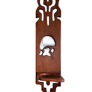 Pode incluir: Um espelho de parede de madeira com uma moldura esculpida decorativa e uma prateleira por baixo. O espelho é retangular e rodeado por um design esculpido. A prateleira é de madeira e está presa à parte inferior do espelho.