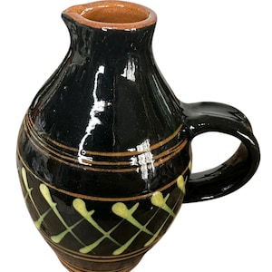 May include: A black ceramic jug with a handle and spout. The jug has a glossy finish with brown and yellow decorative accents. The rim and interior are a natural brown colour. The jug is likely handmade.