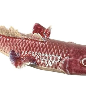 May include: A maroon ceramic fish figurine with a textured scale pattern. The fish has fins, a tail, and a dorsal fin. The figurine is approximately 12 inches long.