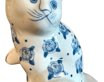 Figura de gato de porcelana azul y blanca sentado con la pata levantada y motivos florales de estilo chino.