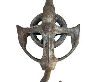 May include: An antique, rusty metal pulley with a hook. The pulley has a wheel in the center and a curved hook at the bottom. The metal has a weathered appearance, suggesting age and use. The pulley is designed for lifting or pulling.