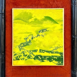 Puede incluir: Obra de arte enmarcada que representa un paisaje con un río y montañas. La obra utiliza una paleta de colores amarillo y verde, con un marco negro estilo bambú y un paspartú de terciopelo rojo.
