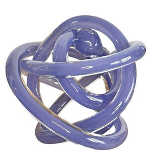 May include: A decorative sculpture crafted from smooth, translucent periwinkle blue glass. The object features a continuous, knotted design formed by a single thick glass tube that loops and intertwines to create a complex, rounded shape.