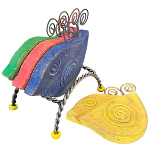 May include: A colorful ceramic bird sculpture with a yellow, red, green, and blue design. The bird is perched on a metal stand with yellow beads. The bird has a whimsical, abstract design.