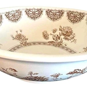 Może przedstawiać: Biała ceramiczna miska z brązowym wzorem kwiatowym. Misa ma szeroki brzeg z ozdobną obwódką i kwiatowymi wzorami. Wnętrze posiada centralny motyw kwiatowy i dodatkowe akcenty kwiatowe.