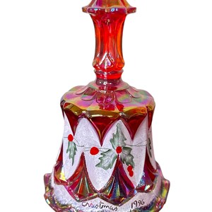 Puede incluir: Una campana de Navidad de vidrio rojo iridiscente con un diseño de acebo pintado en blanco y el texto "Christmas 1996".