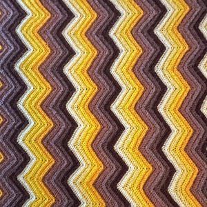 May include: A crocheted blanket with a chevron pattern in shades of brown, yellow, and white.