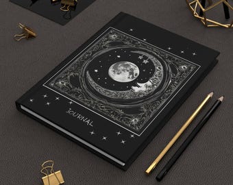 May include: Black journal with a silver crescent moon and stars design. The cover reads "JOURNAL".