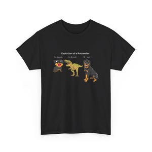 May include: Black t-shirt with a humorous graphic depicting the evolution of a Rottweiler. The graphic shows a Rottweiler puppy, a Rottweiler as a T-Rex, and a full-grown Rottweiler. The text reads "Evolution of a Rottweiler".