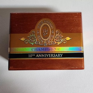 May include: A wooden box with a gold label that says "Perdomo Champagne 10th Anniversary". The label has a gold and red design with a gold seal that says "Perdomo Cabinet Series".