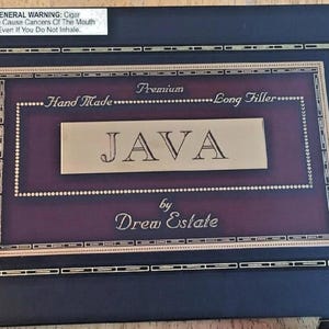 May include: A navy blue cigar box with gold trim and a burgundy interior. The box features the text "JAVA" in a gold rectangular frame, with "Hand Made" and "Long Filler" above. The box is labeled "by Drew Estate".
