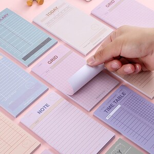 Op de afbeelding: Een verzameling rechthoekige papieren notitieblokken in pasteltinten zoals blauw, roze en paars. Elk blok bevat gedrukte koppen zoals Vocabulary, Today, Grid, Check List, Note en Time Table, met diverse lay-outs inclusief lijnen, rasters en selectievakjes voor organisatie.