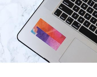 May include: A colorful sticker with a geometric pattern of squares in shades of orange, pink, purple, and blue. The sticker is on a silver laptop.