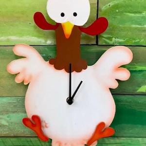 Peut inclure: Une horloge en forme de poulet blanche avec des accents rouges, bruns et jaunes. L'horloge a un pendule et un cadran noir avec des aiguilles noires.