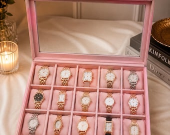 May include: A rectangular pink velvet watch display case with a clear glass lid and silver metal latches. The interior features fifteen individual compartments, each containing a watch resting on a soft pink velvet cushion, showcasing various styles.