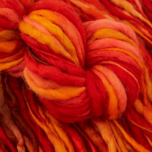 Puede incluir: Un primer plano de un ovillo de hilo en tonos rojos, naranjas y amarillos. El hilo es suave y esponjoso, y es perfecto para tejer o hacer ganchillo.
